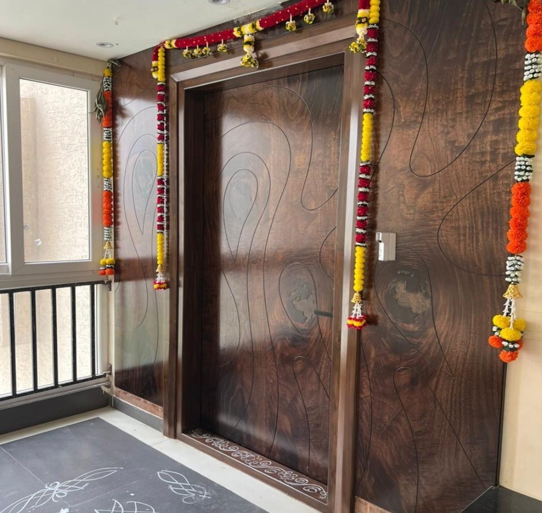 Carved walnut entrance door with floral garlands and a kolam on stone