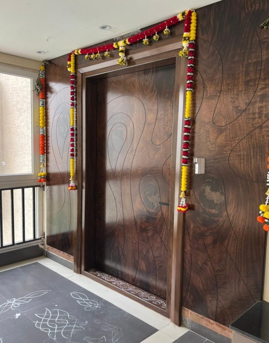 Carved walnut entrance door with floral garlands and a kolam on stone