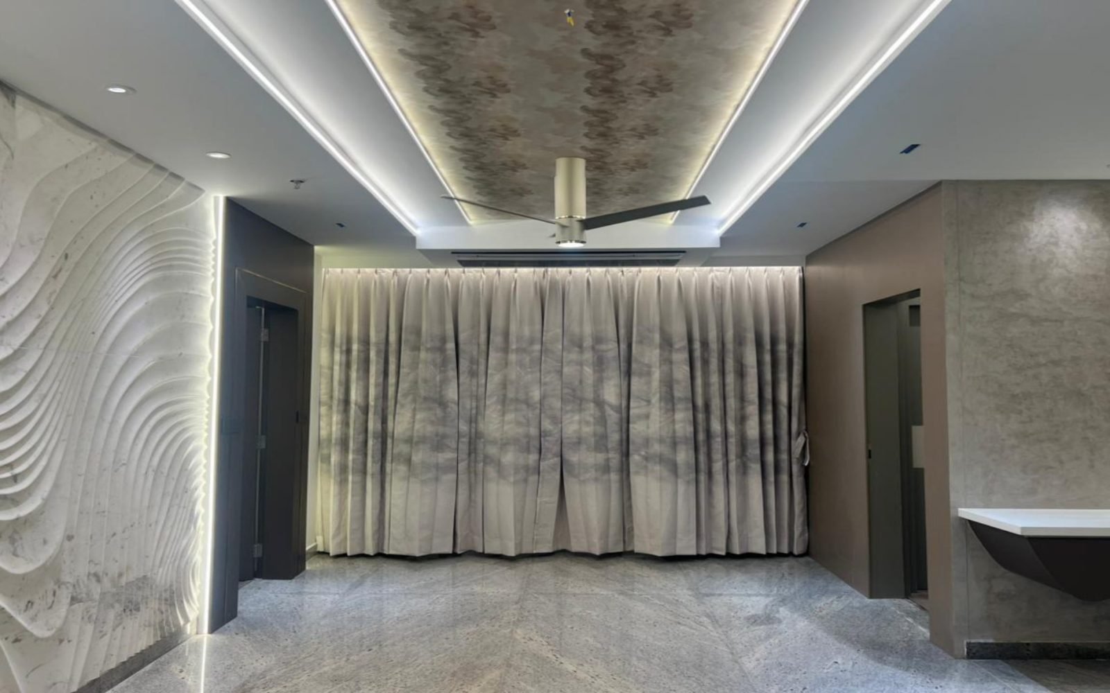 Living hall with carved wave marble, floor-to-ceiling drapery, and linear ceiling light