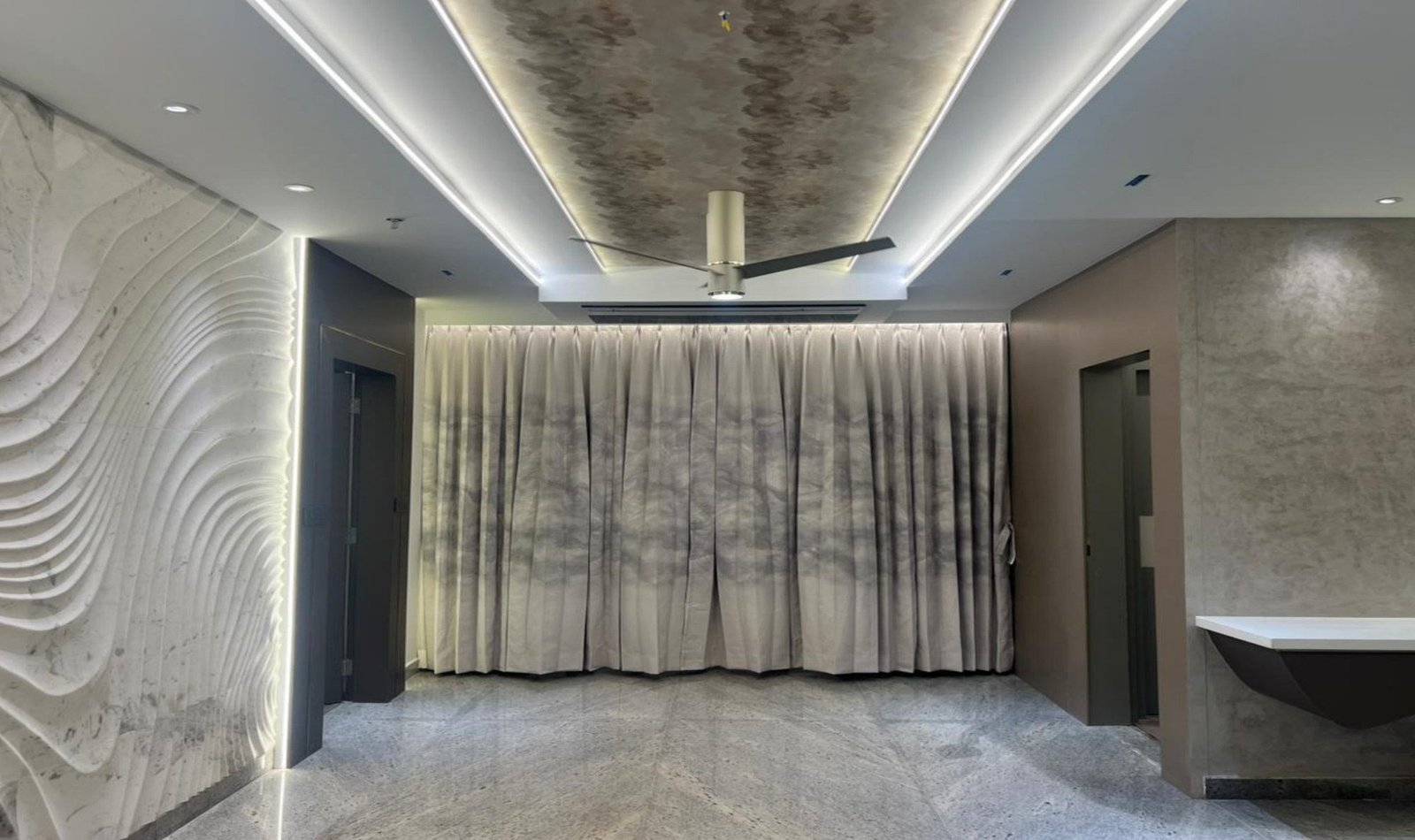 Living hall with carved wave marble, floor-to-ceiling drapery, and linear ceiling light