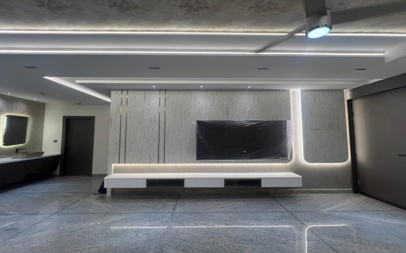 Media wall in pale stone with floating console and grazed lighting