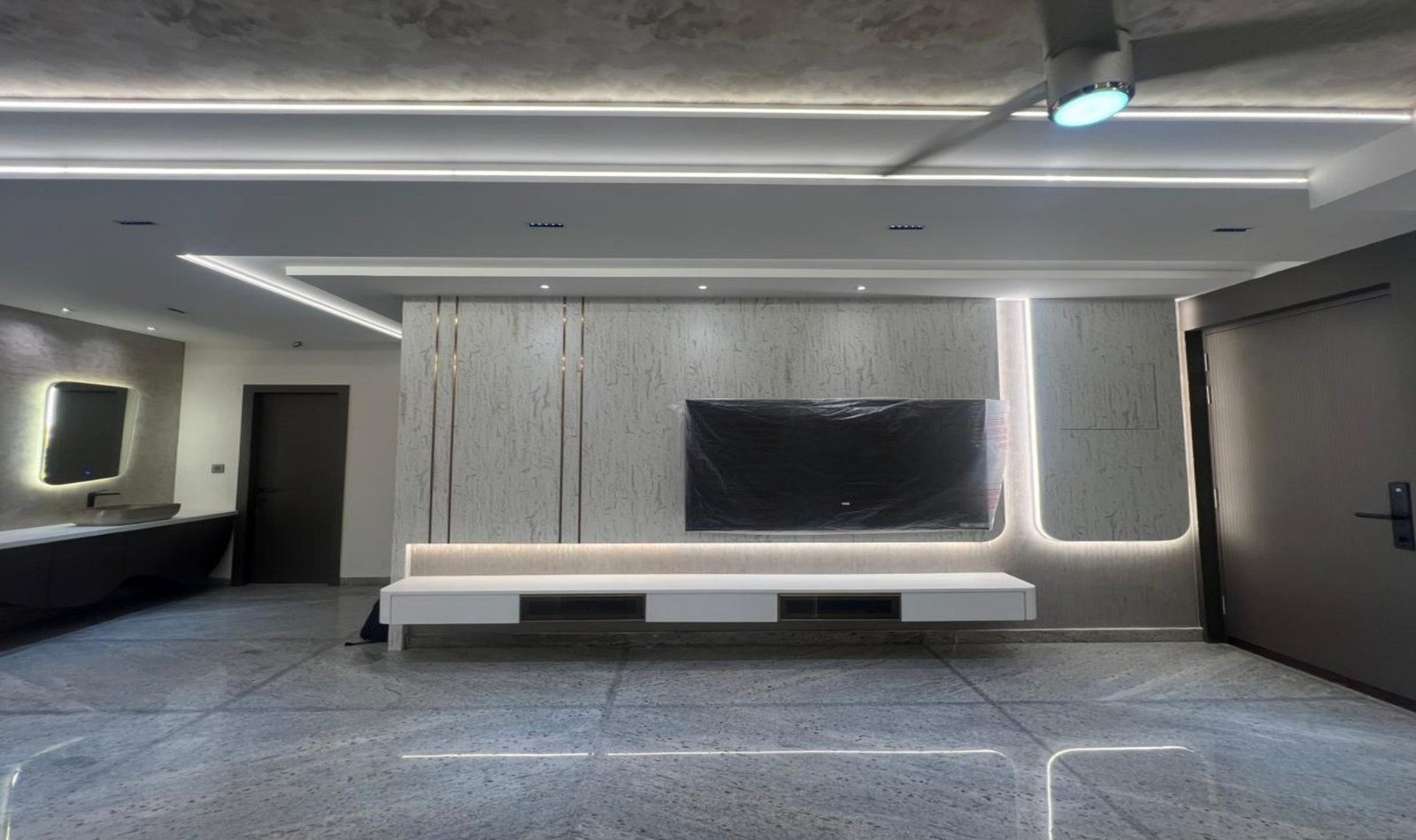 Media wall in pale stone with floating console and grazed lighting